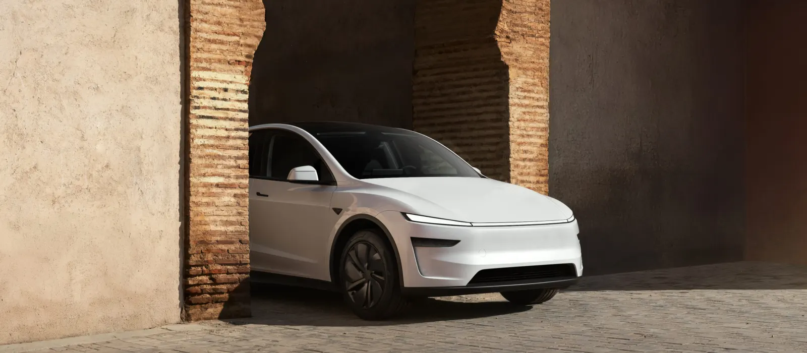 Tesla Model Y blanco aparcado bajo un arco de piedra mediterráneo